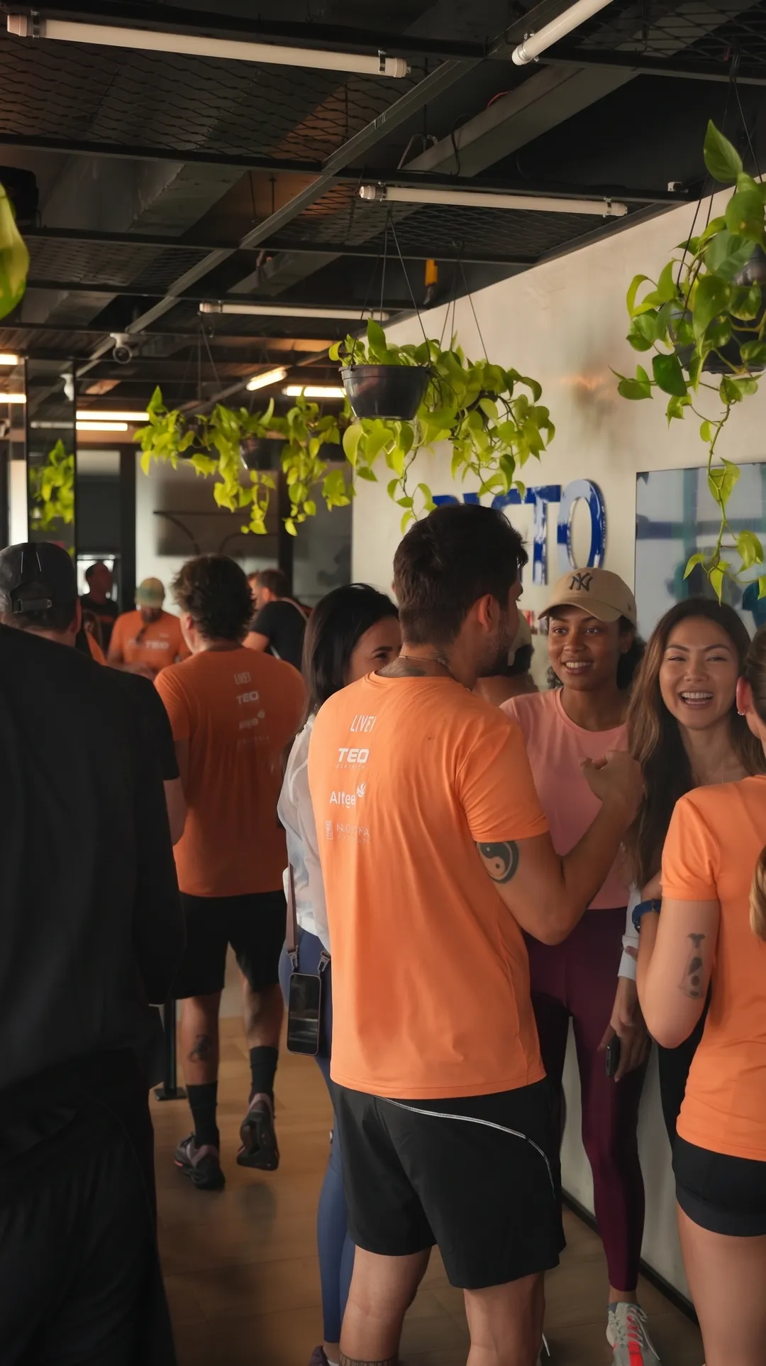 Pessoas com camisetas laranja da Teo conversando no espaço de convivência, com a marca Pacto ao fundo